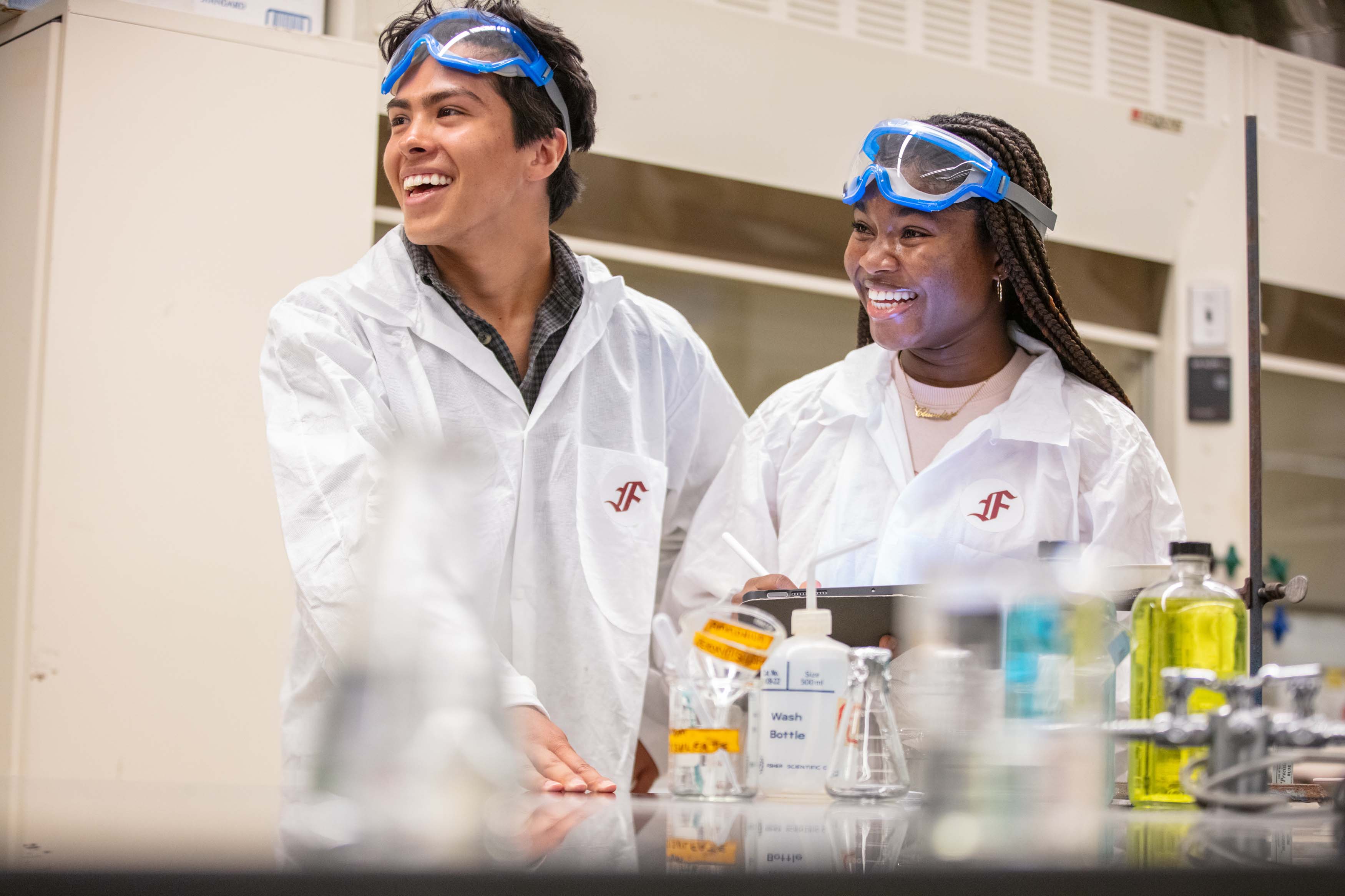 two students smiling in lab with goggles and equipment