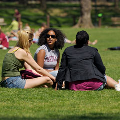 Three students sit together on the lawn in front of Keating Hall on a sunny day