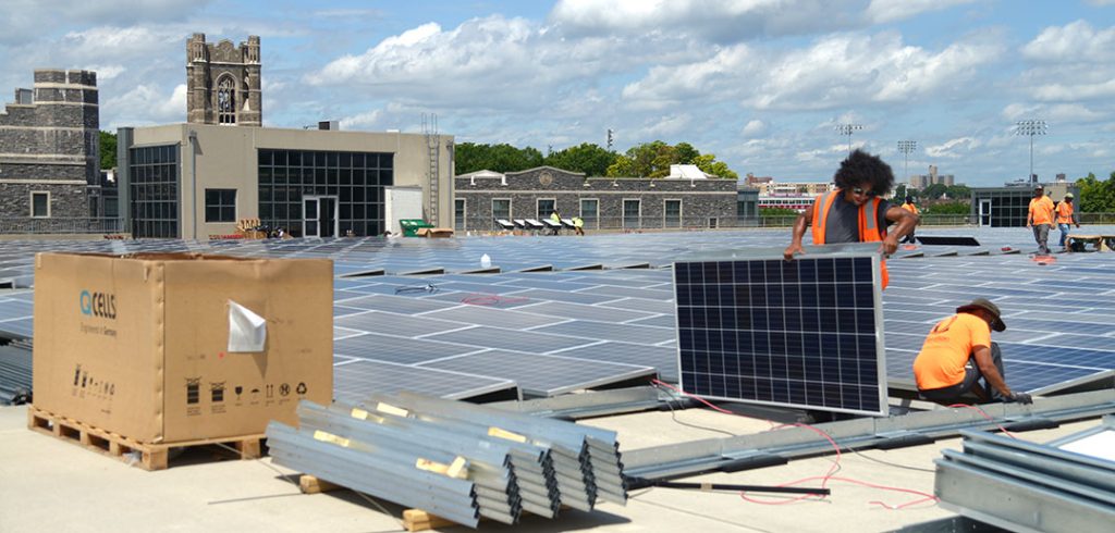 Two workers installing solar panels on a roof