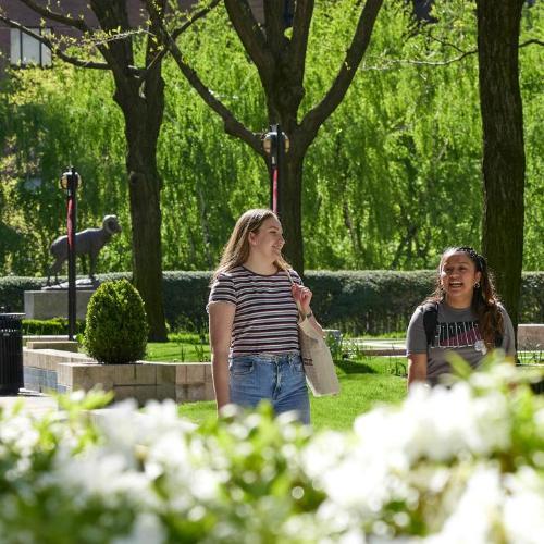 Two students at the Lincoln Center campus walk along the plaza in the summer