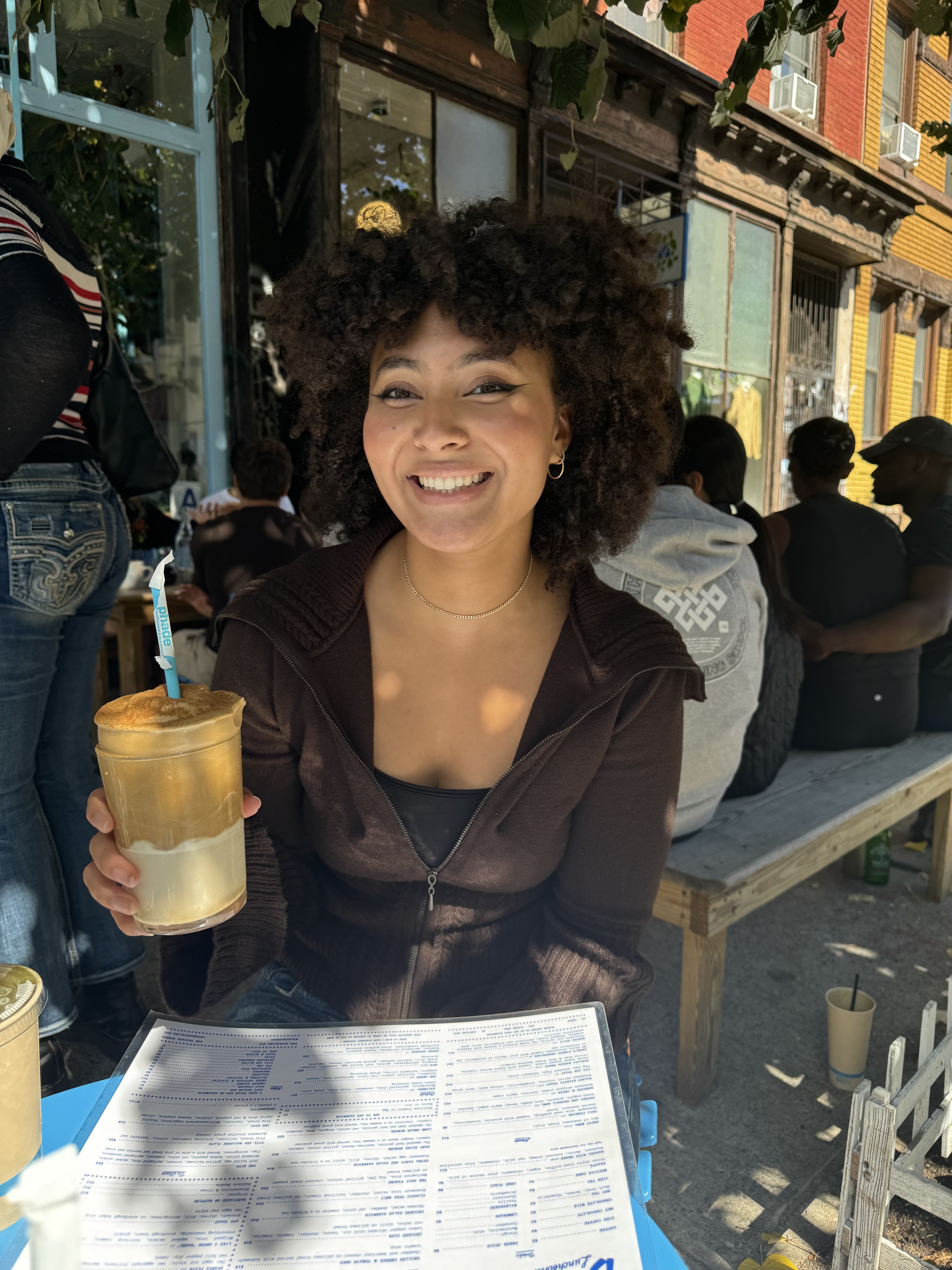 Christophene sitting outside in a cafe holding a iced coffee