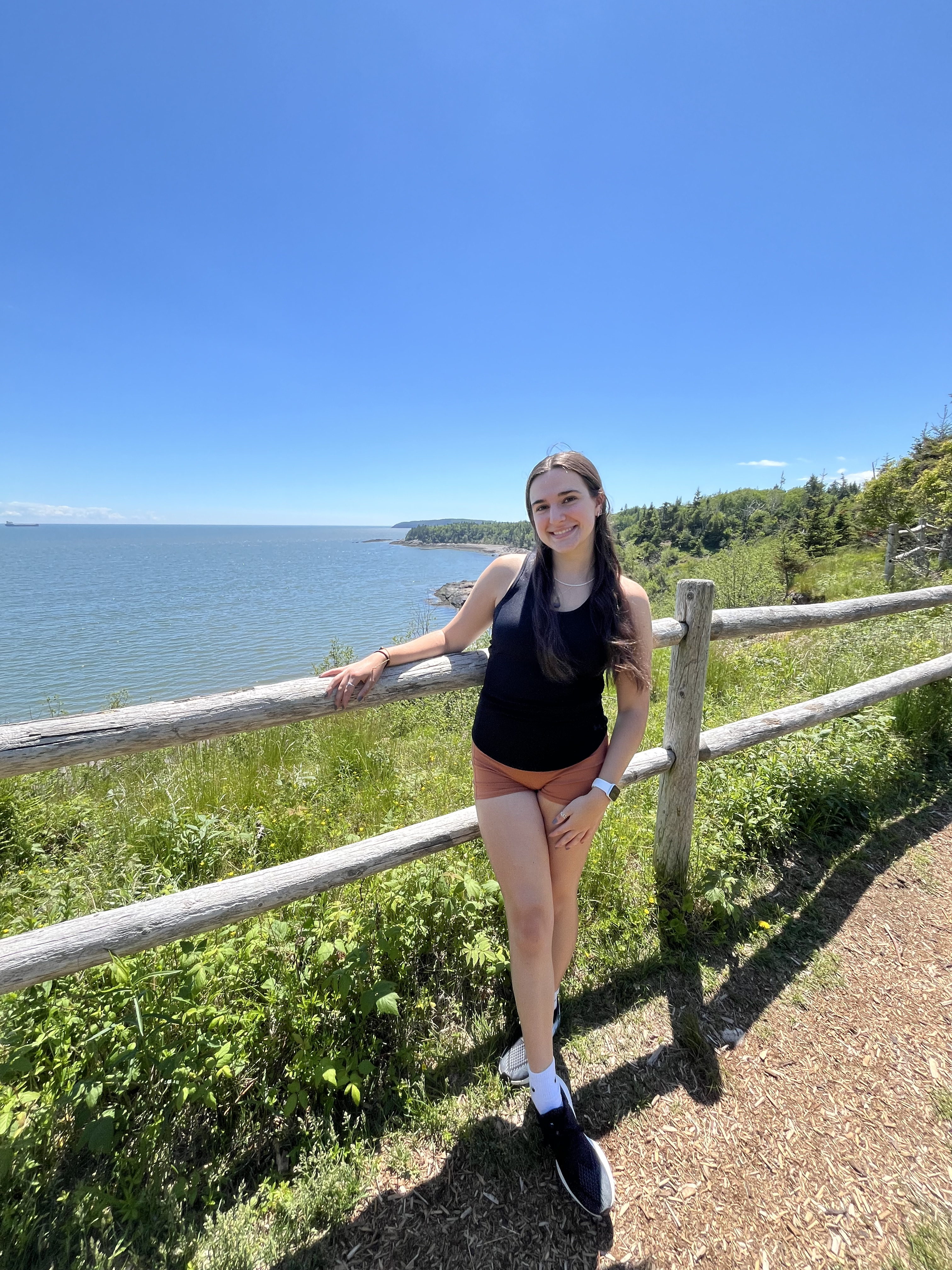 Megan standing on a path in front of a wooden fence in front of the ocean