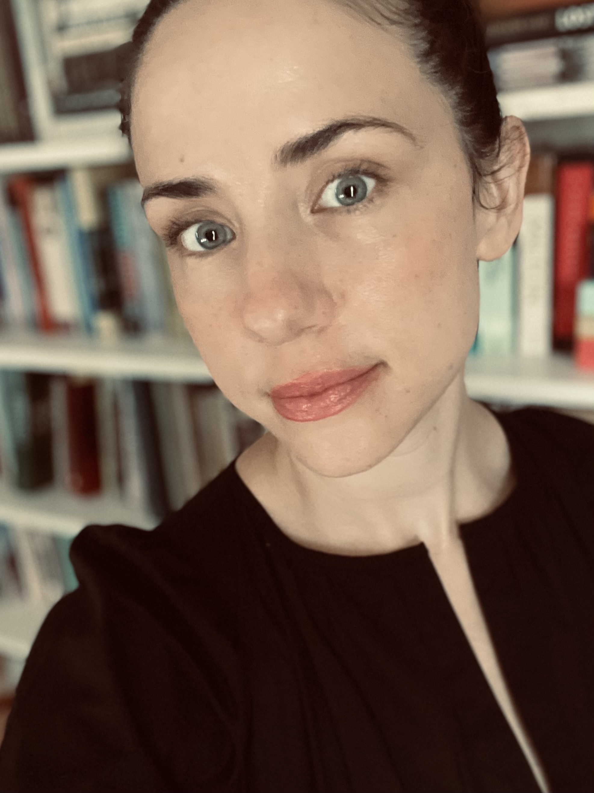 A headshot of Brianne Jacobs, a 2017 PhD graduate of Fordham's Theology Department. Jacobs is wearing a black shirt in front of a bookshelf full of books.