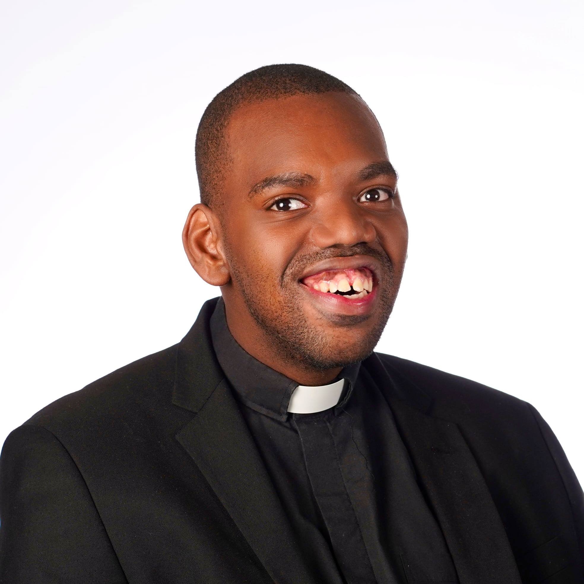 A headshot photo of Kyle Stevenson, a doctoral student in the theological and social ethics track in the Theology Department at Fordham University. Kyle is wearing a clerical collar with a black dress shirt and black suit jacket