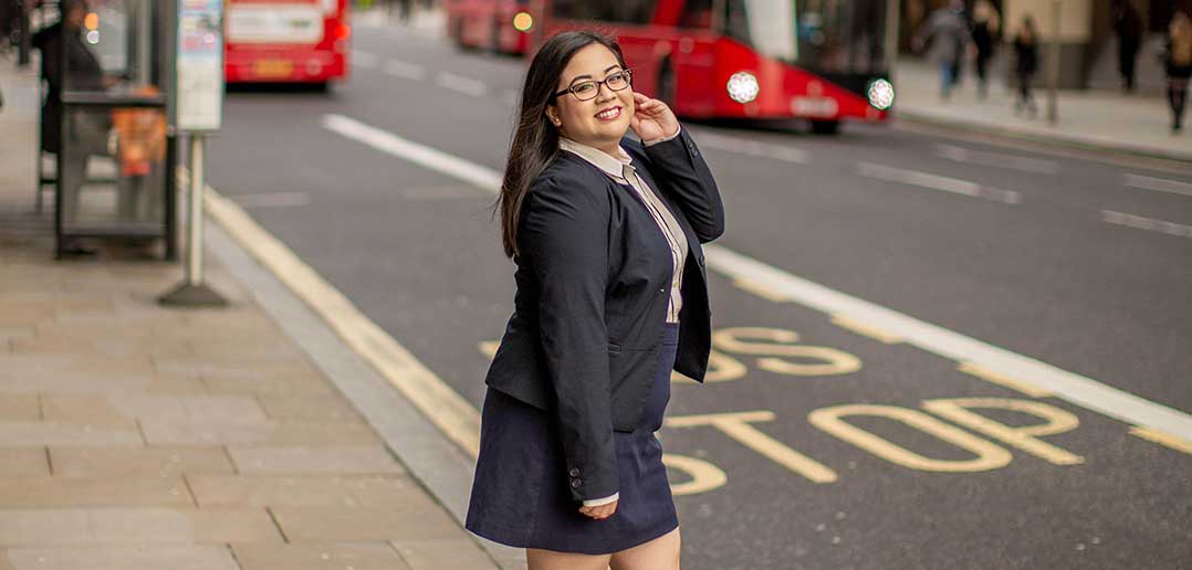 Young woman with dark hair standing on a sidewalk.