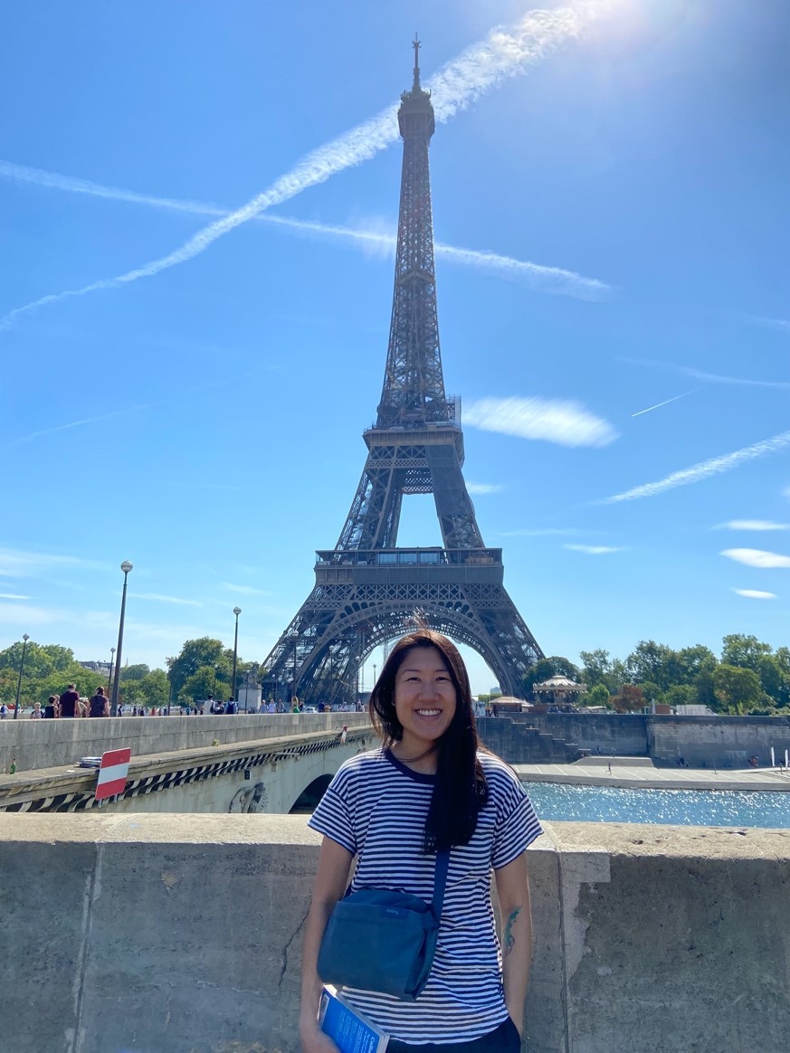A photo of Shela Chan, a doctoral student in the theological and social ethics track in the Theology Department at Fordham University, standing in front of the Eiffel Tower on a sunny day