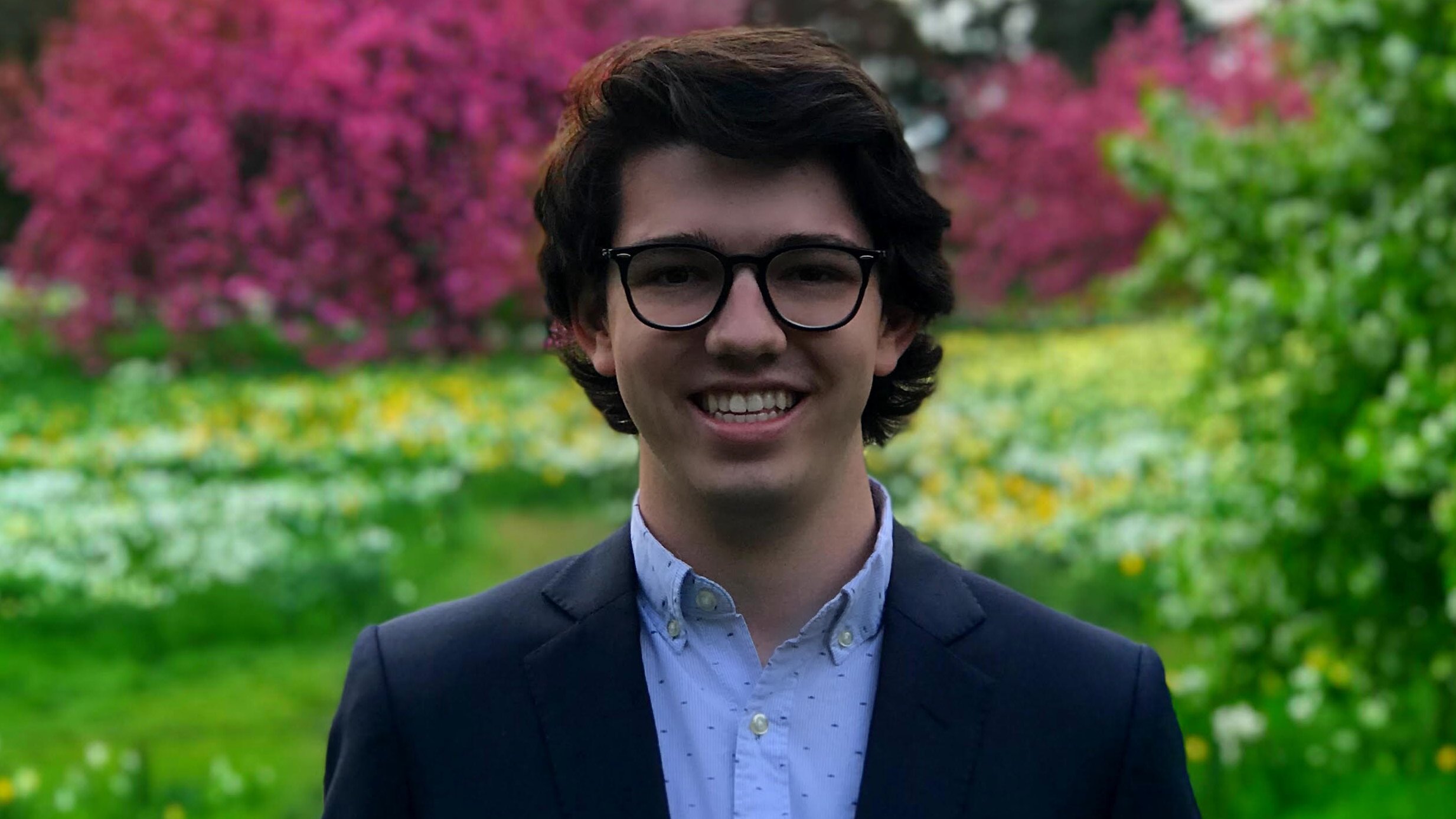 Young man with brown hair and glasses wearing a blue shirt.