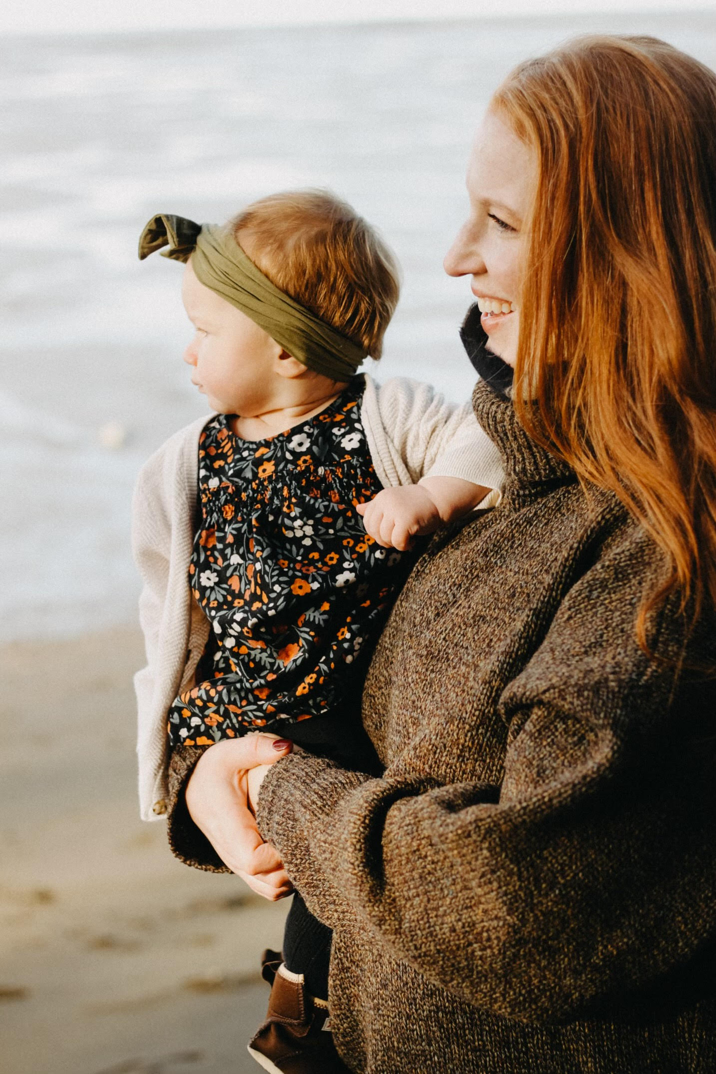 Young woman with red hair holding baby at the beach.