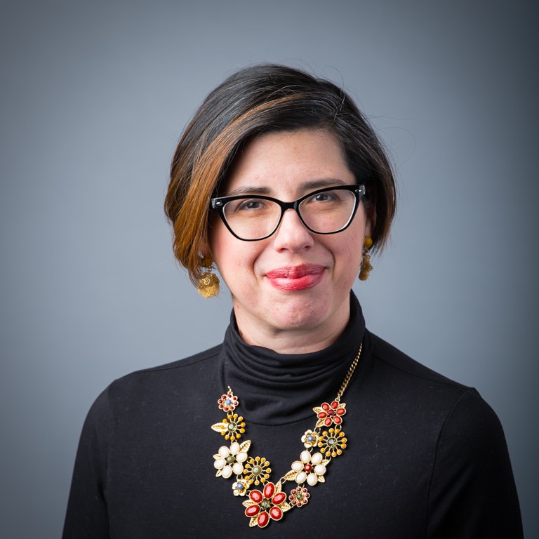 Young woman in black shirt with glasses and floral necklace.