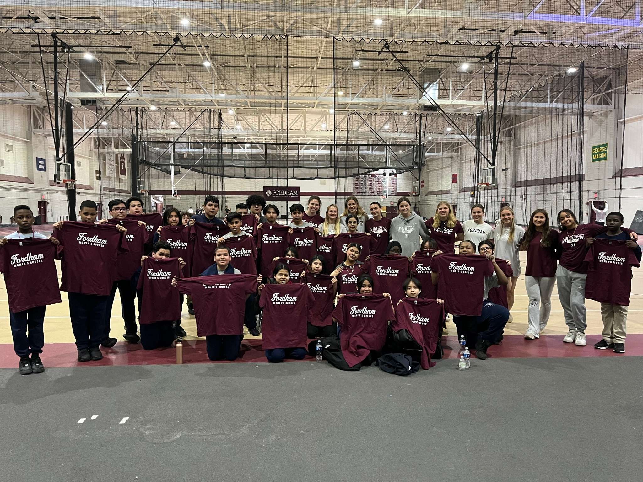 large group of students gathered holding Fordham women's soccer T-shirts