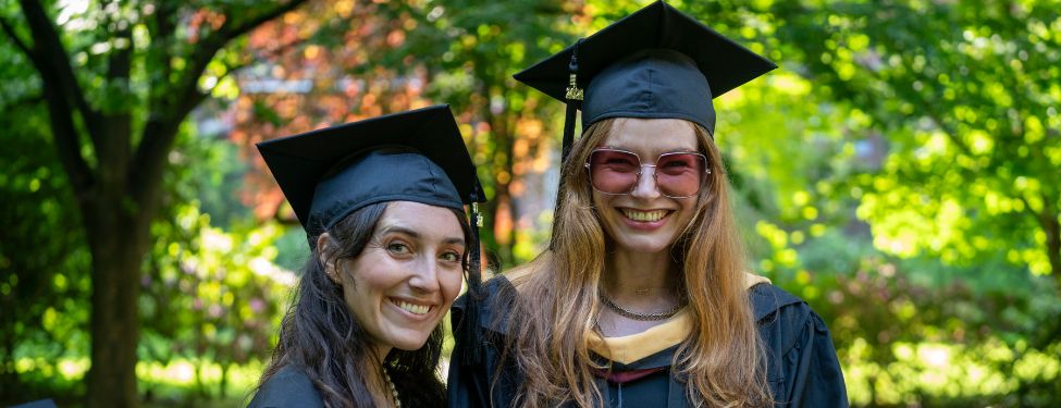 Two MSW students pose for a photo in their cap and gowns on graduation day.