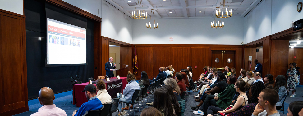 The 12th-Floor Lounge of Fordham's Lincoln Center campus, crowded with people watching someone speak at an event.